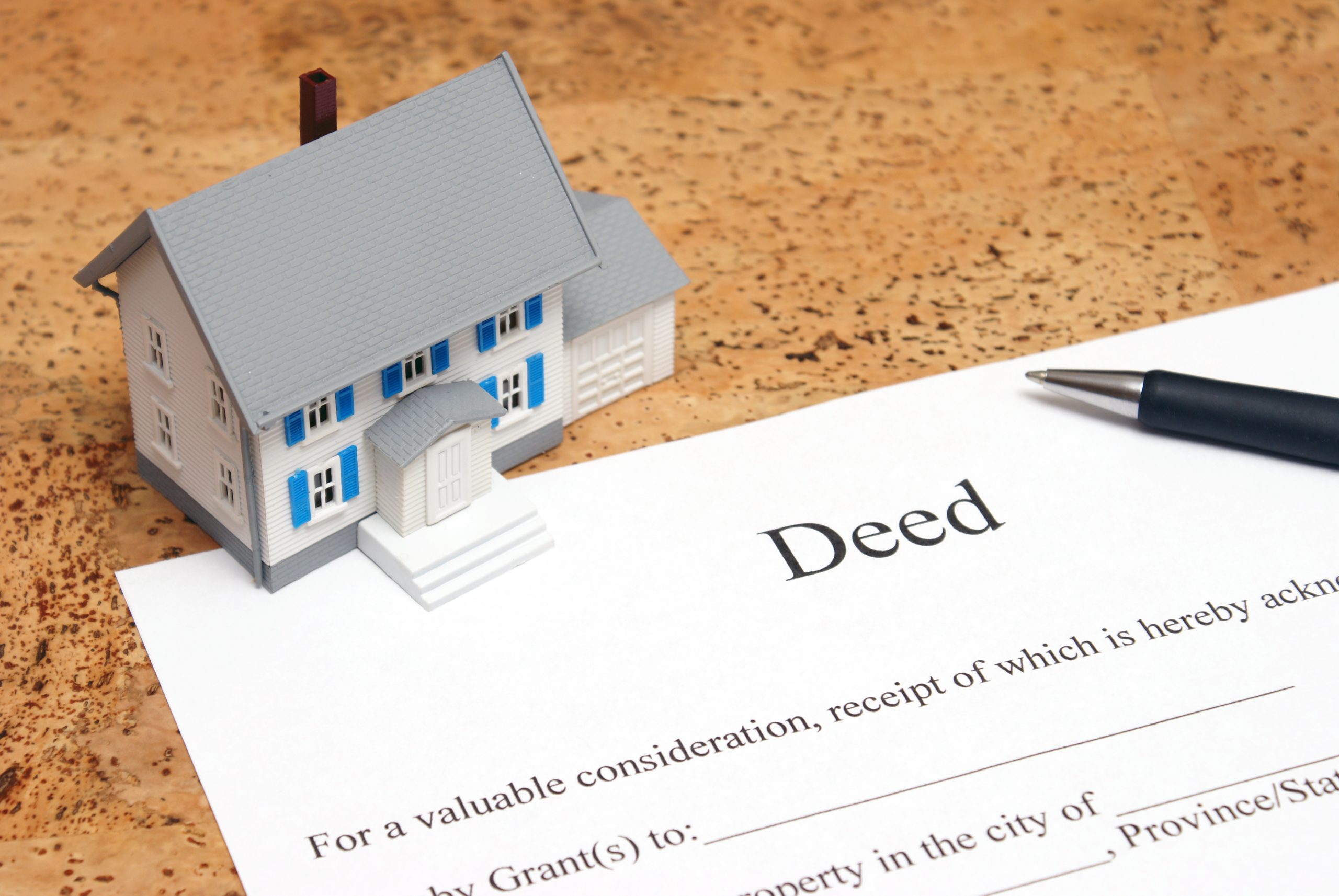 a small model of a house covering the top of a piece of paper titled "Deed" with a pen sitting on top of it.