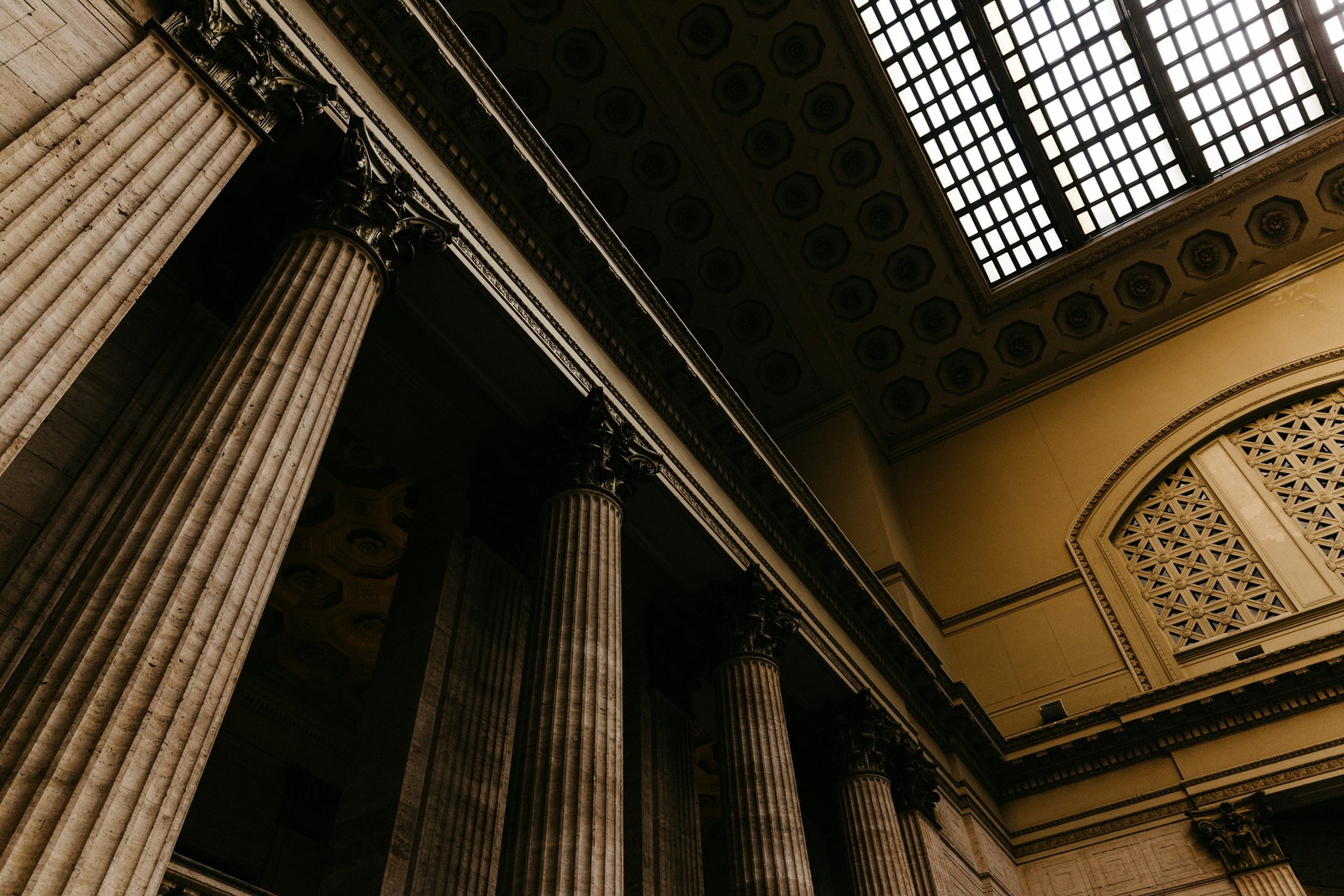 Angled shot of the inside of a court house with four columns on the left and a windowed ceiling to the top right allowing light into the room. Photo by Patrick Fore on Unsplash.