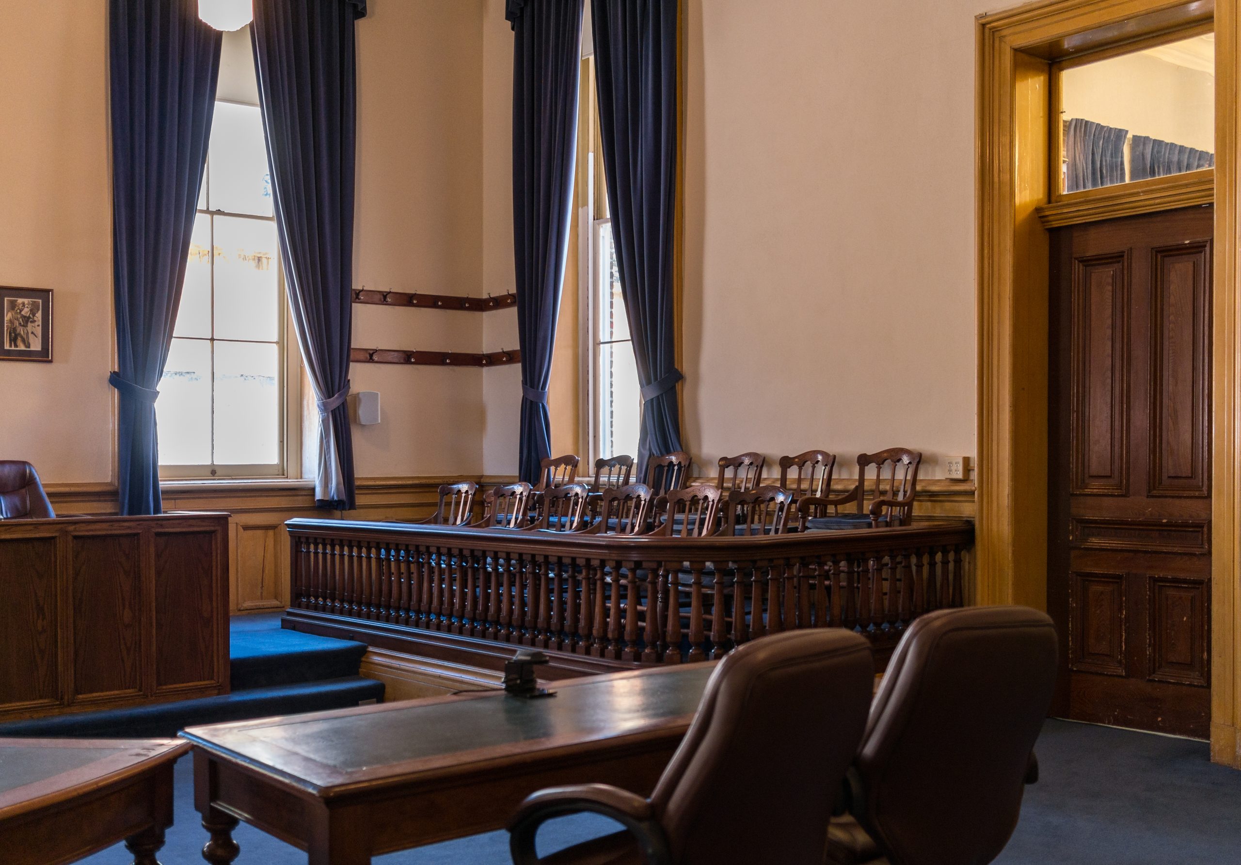 inside of an empty jury room with many wooden chairs in front of the jury box, an empty desk with two chairs in the foreground, and a witness stand.