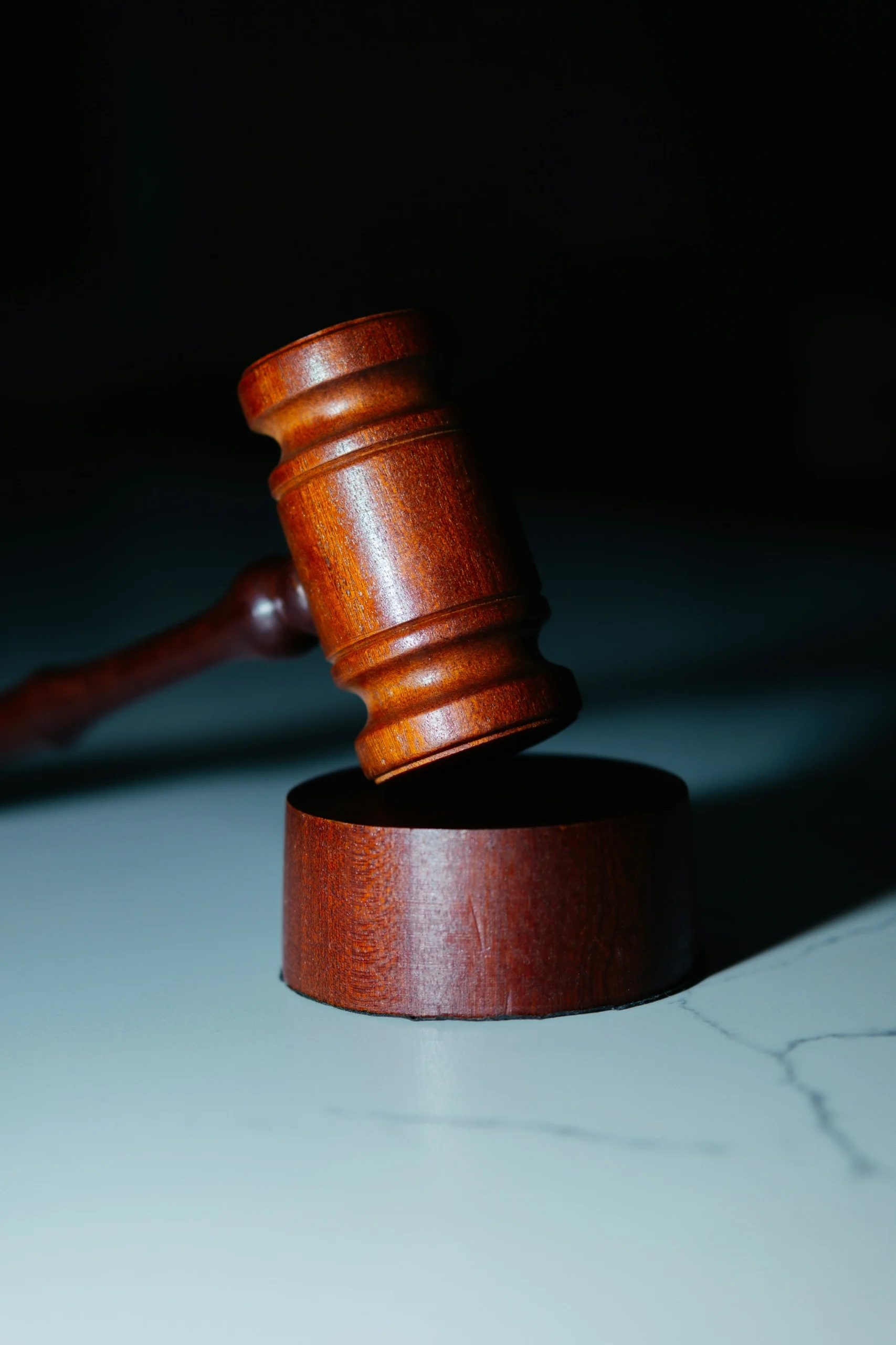 Wooden gavel coming down on block on a marble desk with shadows behind it. Photo by Wesley Tingey on Unsplash